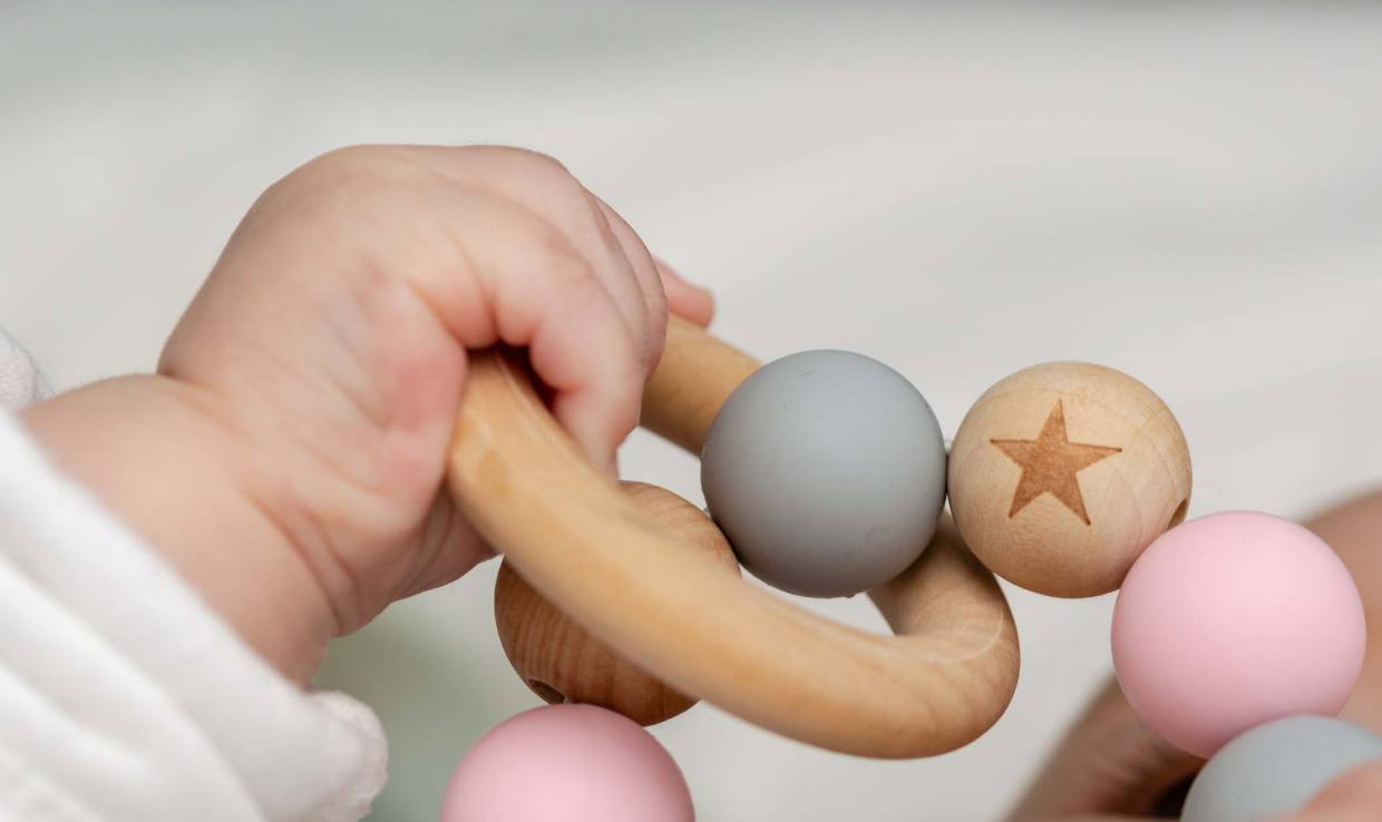 Close-up of a baby’s hand gripping a wooden ring toy with pastel beads